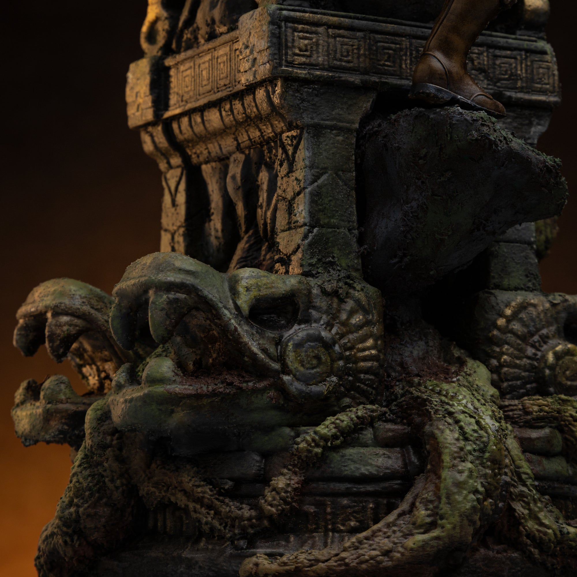 A detailed close-up of the base of the Lara Croft statue, showing moss-covered stone snake heads and thick vines.
