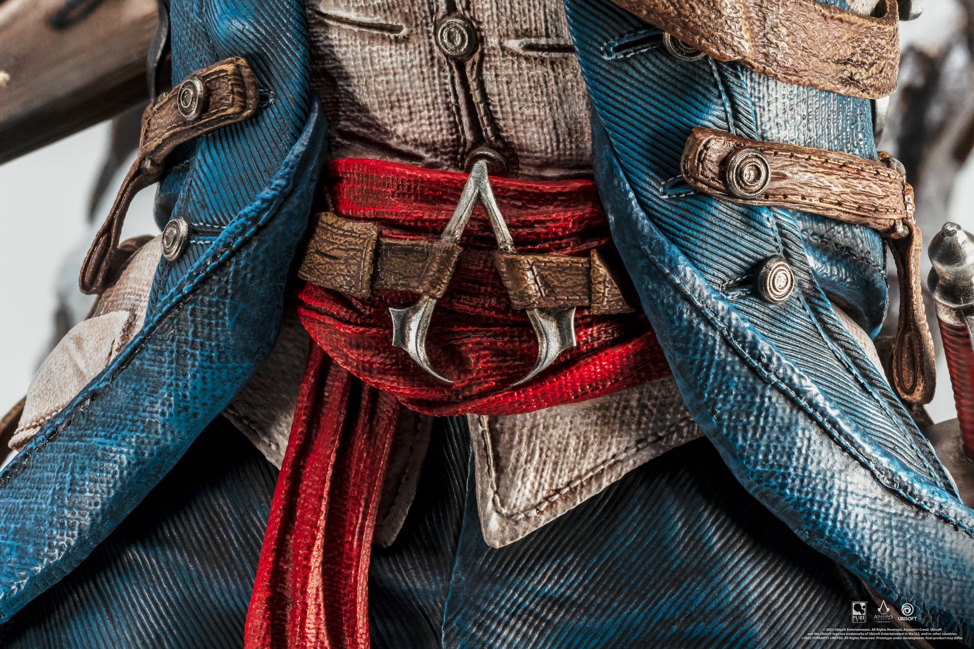 An extreme close-up of the midsection of the Animus Connor statue, focusing on the red sash and the classic Assassin's Creed logo on his belt buckle.