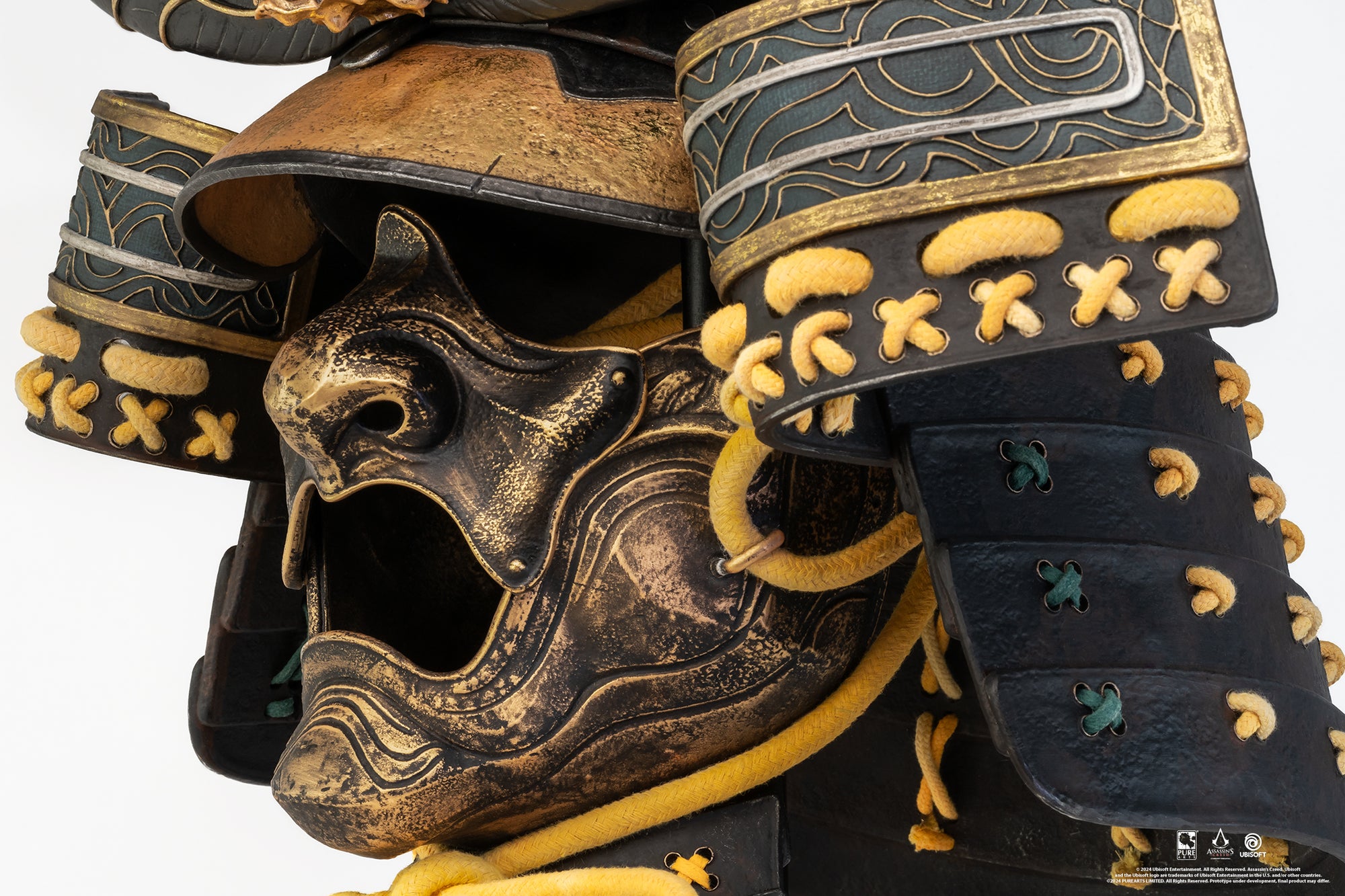 Detailed close-up of the left side of the PureArts Yasuke helmet's mask, showcasing the textured gold finish, rope ties, and the layered armor plates of the neck guard.