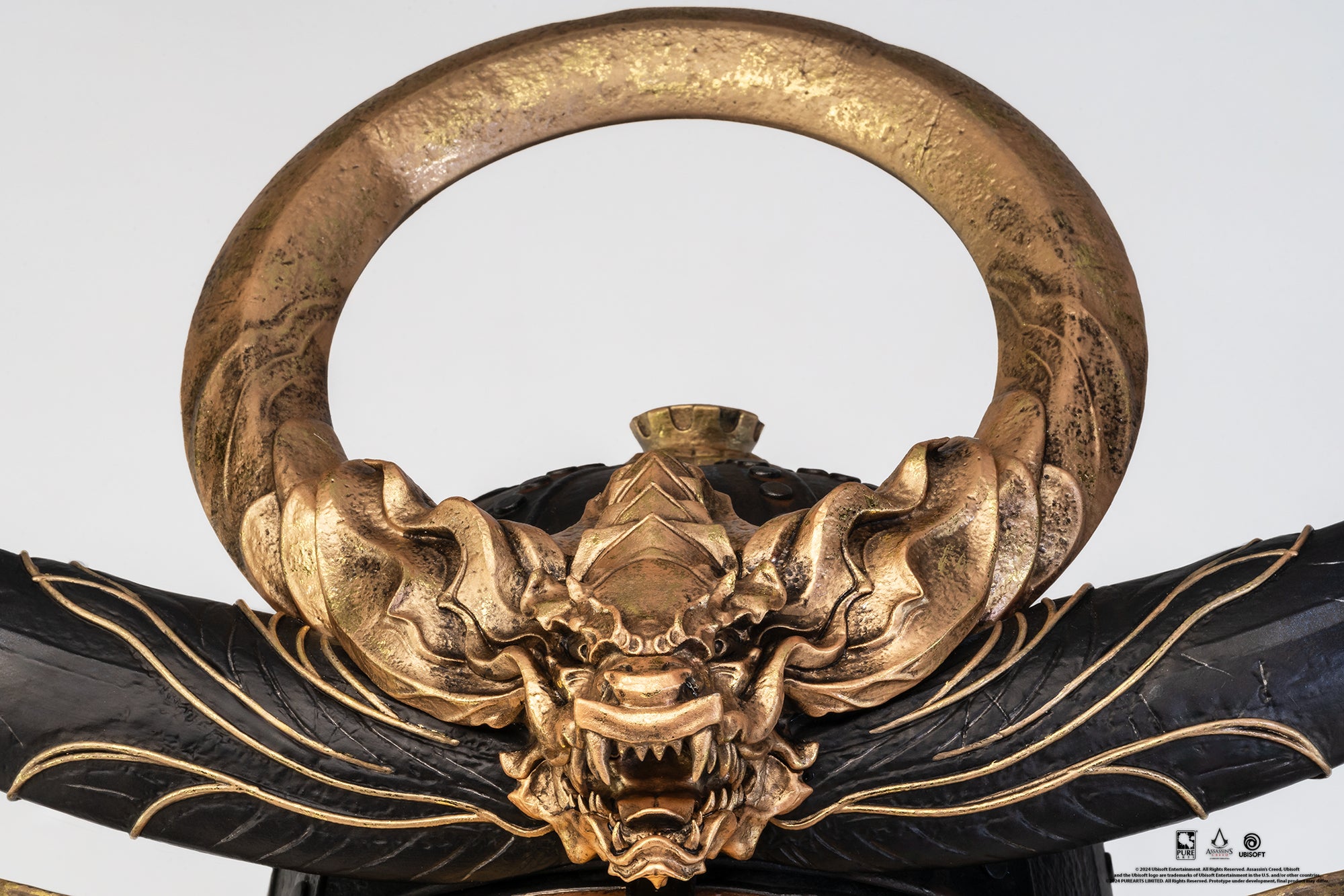 A close-up view of the intricate gold crest on the PureArts Yasuke helmet replica, featuring a detailed, fierce dragon and a prominent circular ring.