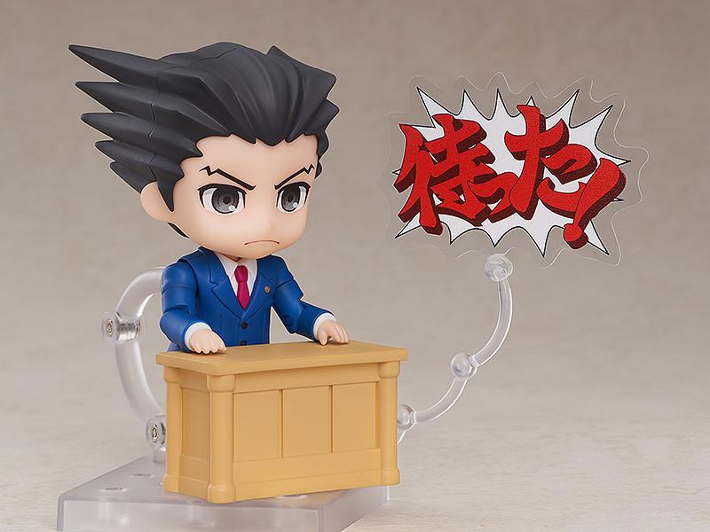 Phoenix Wright Nendoroid figure behind wooden courtroom desk with court document.