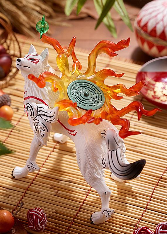 High-angle overhead shot of the Okami Amaterasu figure on a bamboo surface, accentuating the circular pattern on the green reflector and the spreading flame trail.