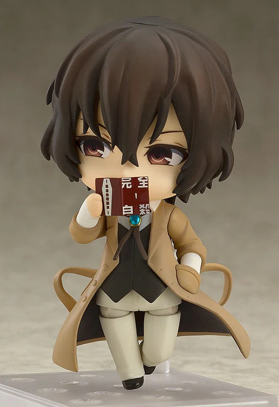 Nendoroid Osamu Dazai figure holding his book up to cover the lower half of his face, with a thoughtful/mischievous expression.