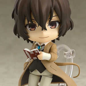 Nendoroid Osamu Dazai figure with the standard face, holding his book and wearing his tan trench coat and bandage-wrapped wrist.
