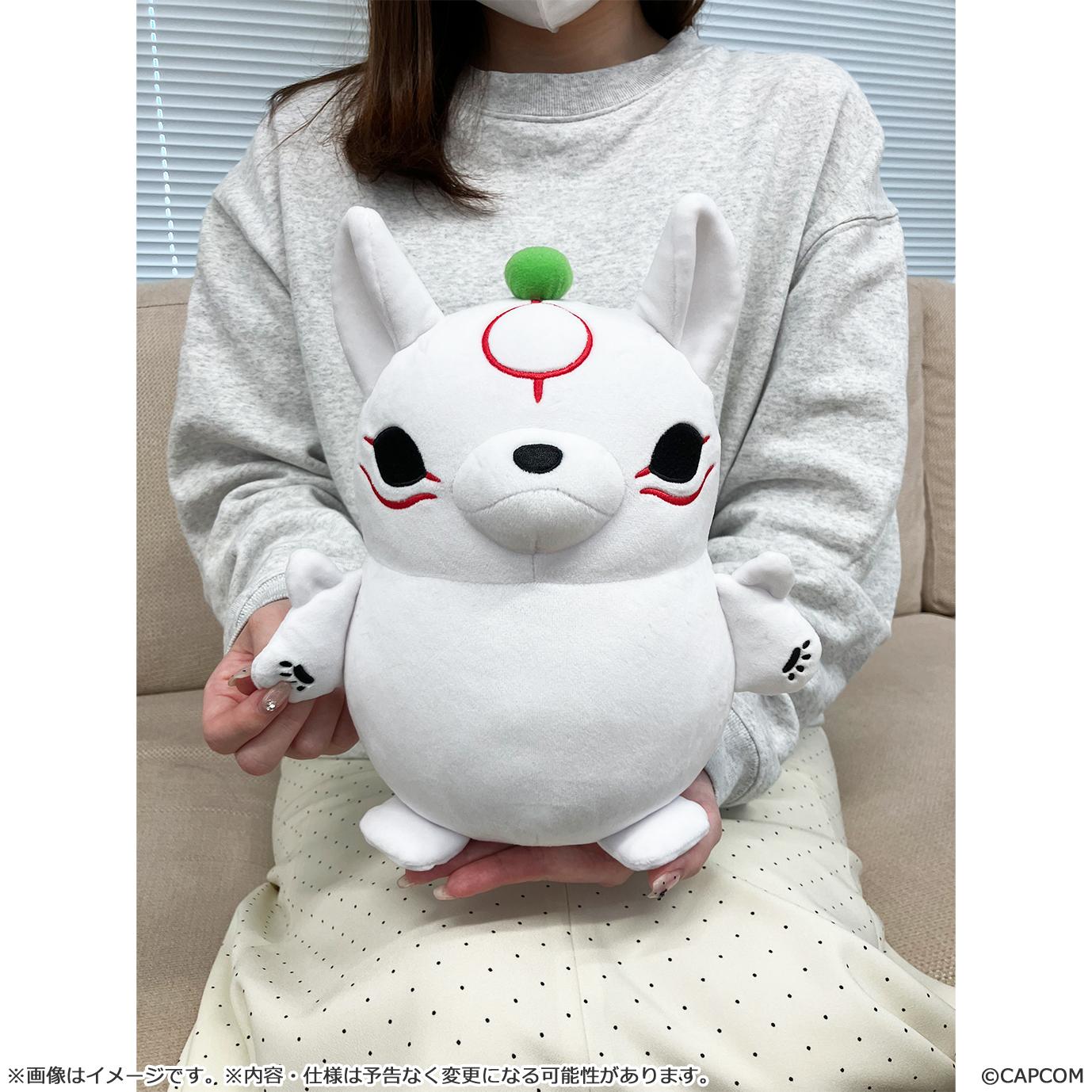 Size reference shot showing a person holding the 10.82-inch medium size Okami Amaterasu MochiKawa plush toy in their lap to demonstrate its scale.