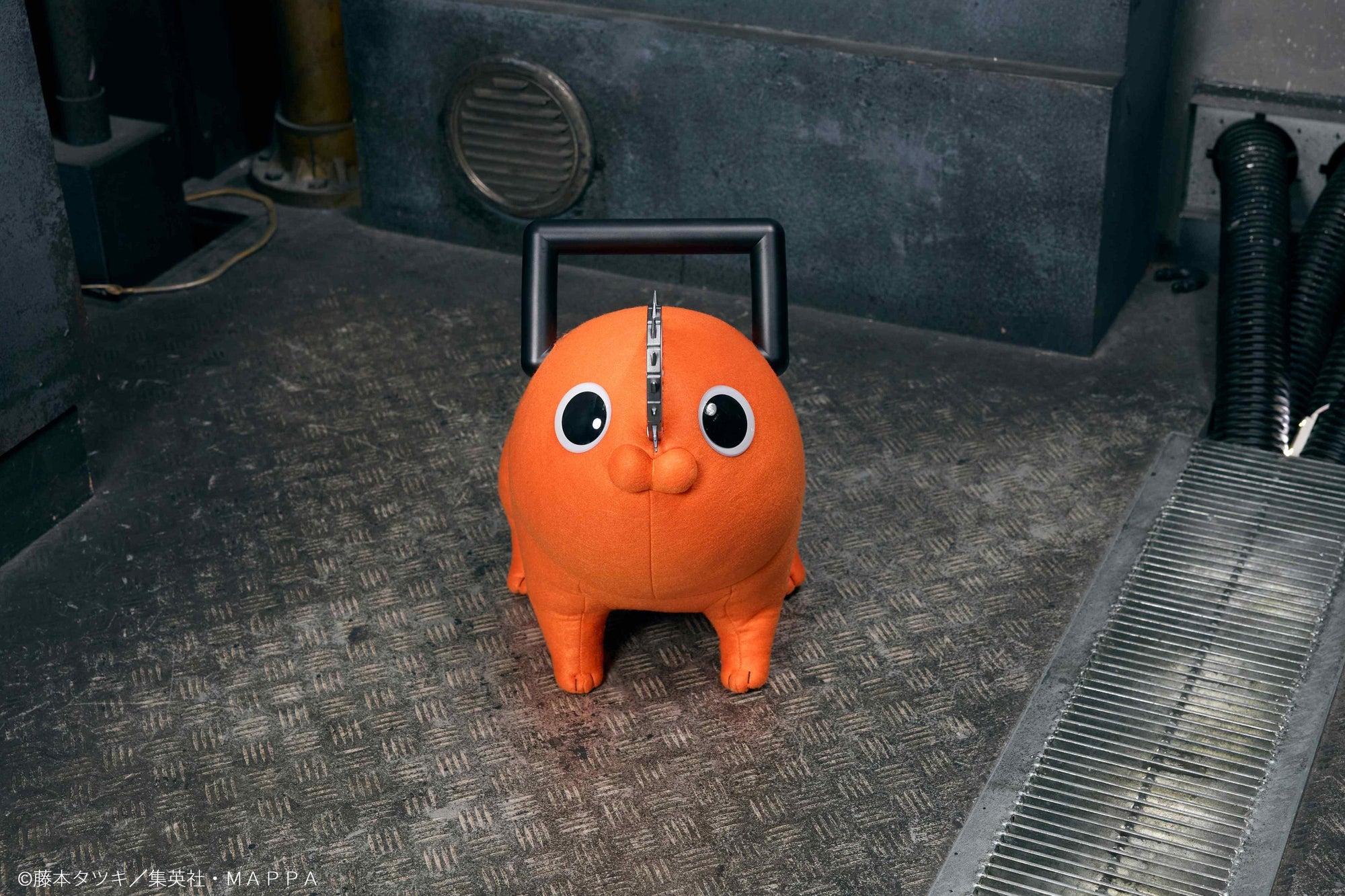 Frontal head-on view of the Pochita life-size plush doll sitting on industrial metal flooring.