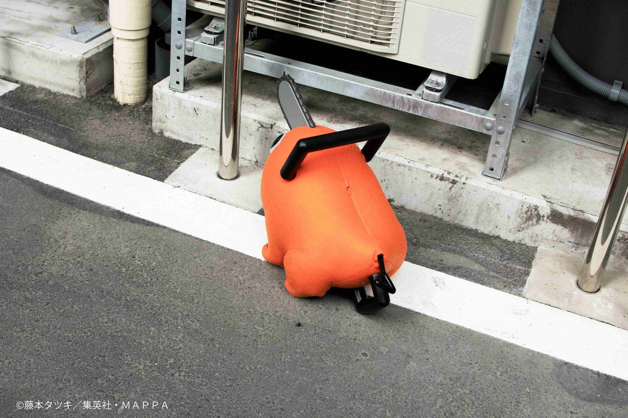 Back view of the Pochita life-size plush doll sitting on pavement outdoors.