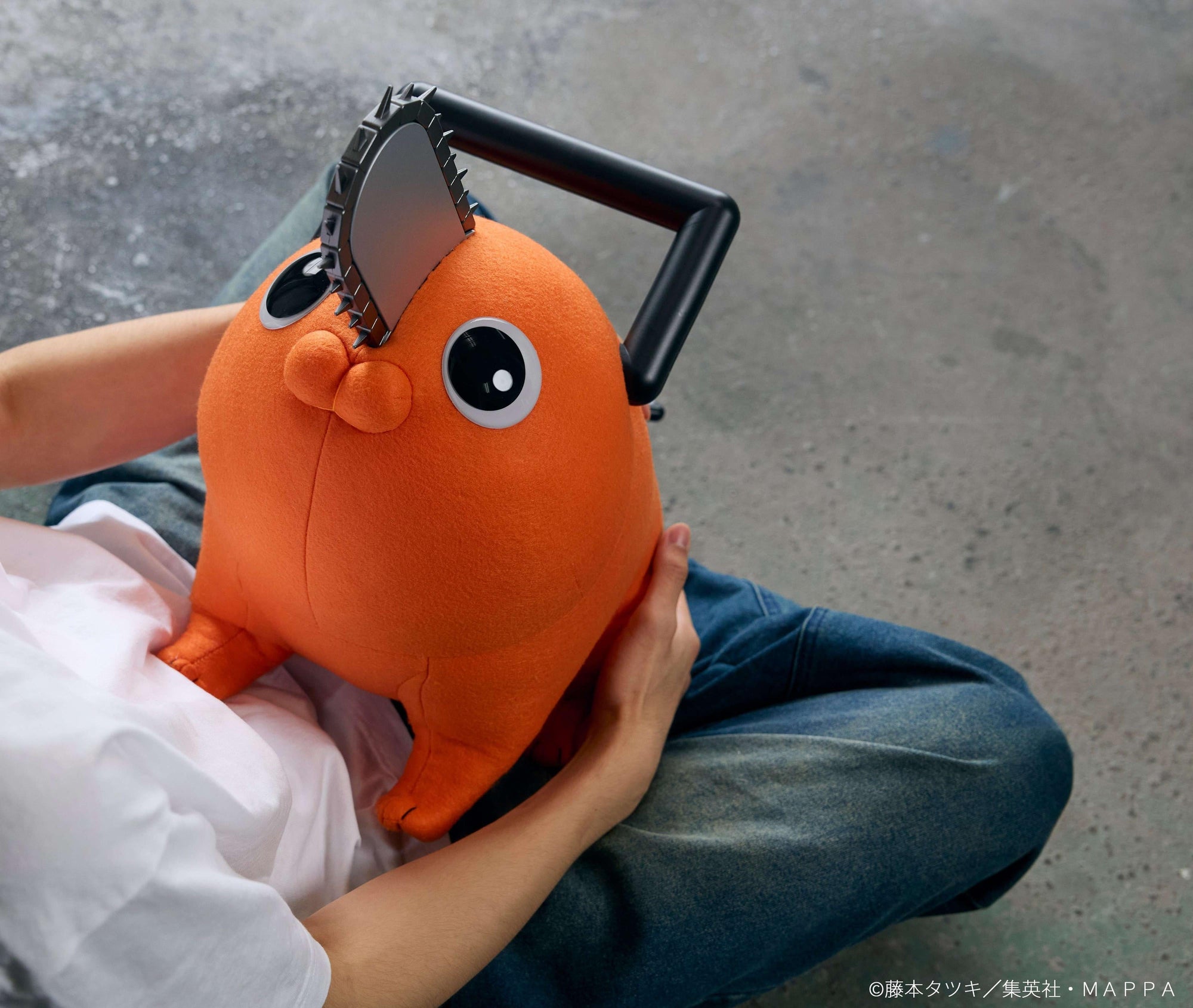 Overhead shot of a person cradling the Pochita life-size plush doll while seated on the floor.