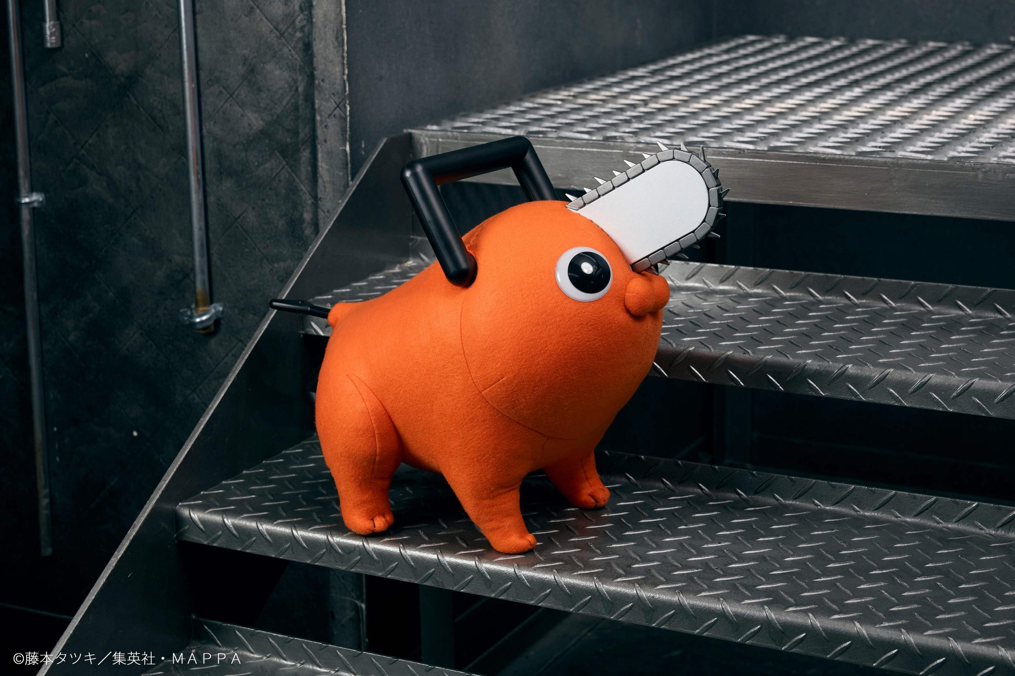 Angled front view of the Pochita life-size plush doll looking upward on diamond plate metal stairs.