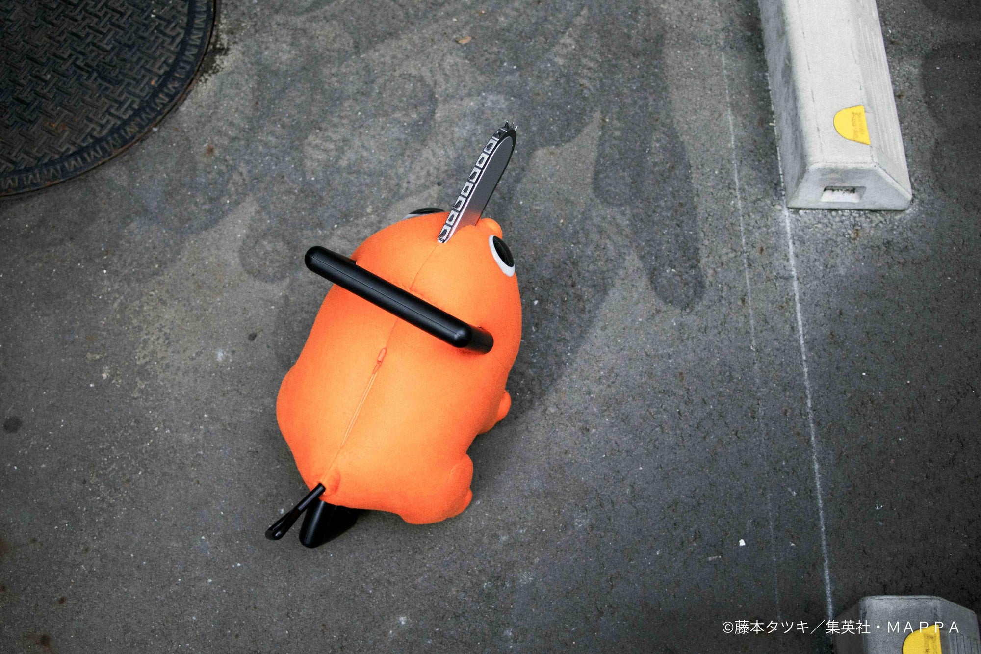 Top-down angle view of the Pochita life-size plush doll standing on outdoor pavement.