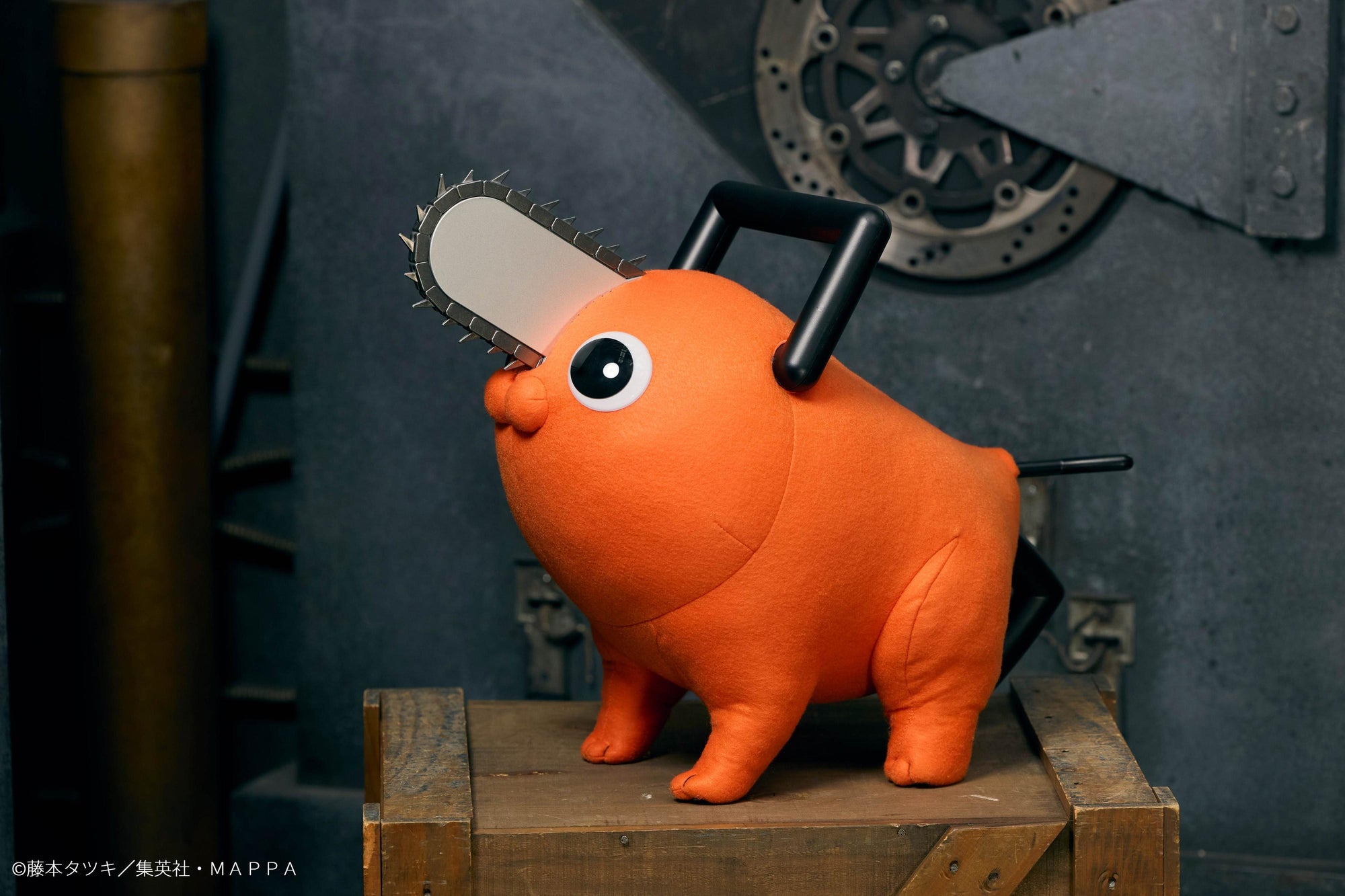 Pochita life-size plush doll standing on a wooden crate against an industrial gear backdrop.