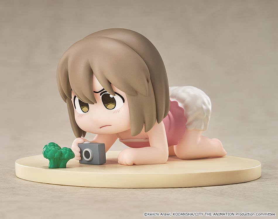 Studio display view of the non-articulated Niikura Mini Memory collectible anime figure crawling with a toy camera and miniature broccoli.