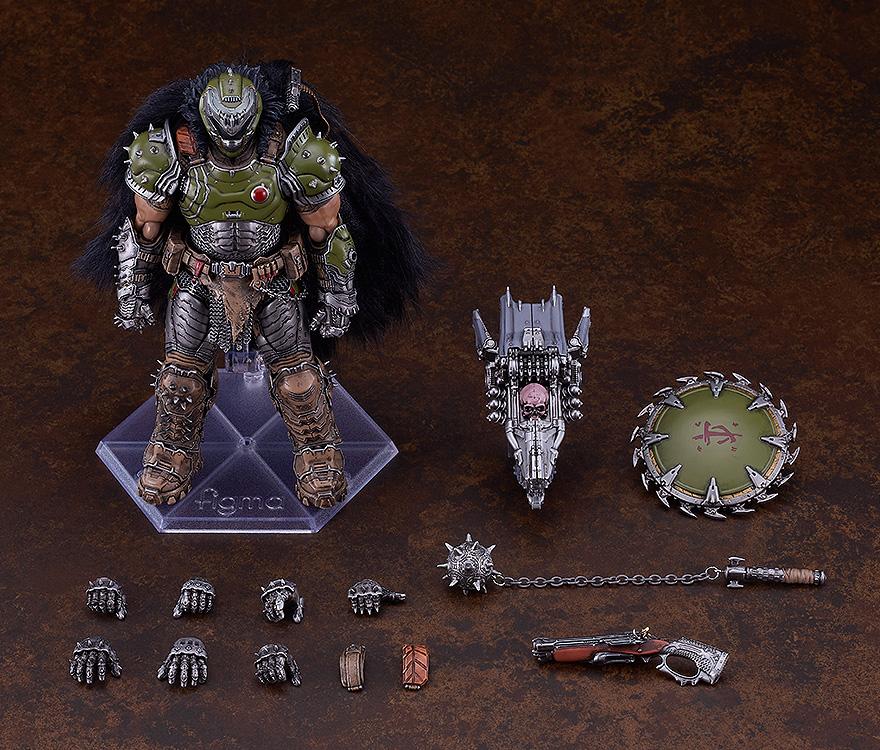 Overhead studio layout of the figma Doom Slayer DX Edition contents, showing the figure, interchangeable hands, cape attachments, super shotgun, spiked flail, chain shield, and skull crusher weapon.