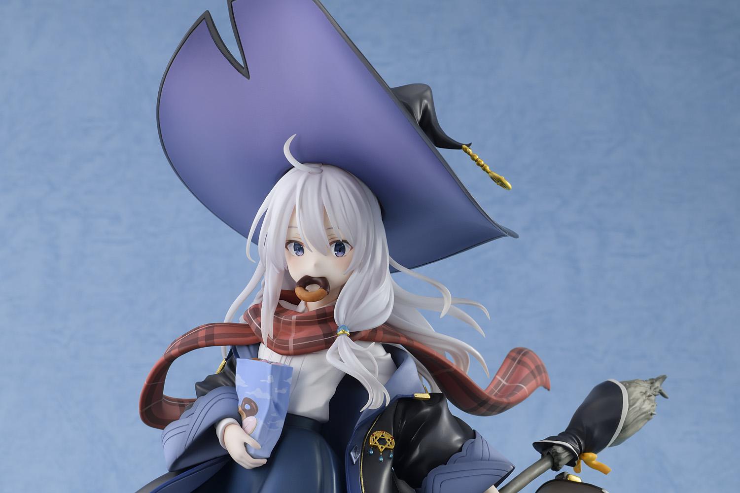 Close-up upper body shot of the Elaina scale figure wearing her pointed witch hat and eating a donut while holding a blue snack bag.