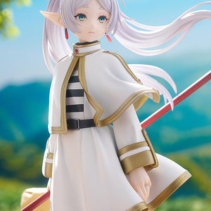 Promotional lifestyle image of Frieren the mage standing in a lush green meadow under a blue sky.