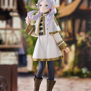 Full-body three-quarter angle of the Frieren elven mage figure posed within a detailed medieval fantasy town layout under a blue sky.