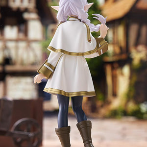Back view of the Frieren POP UP PARADE figure in a scenic outdoor village diorama, emphasizing the flow of her capelet and hair.