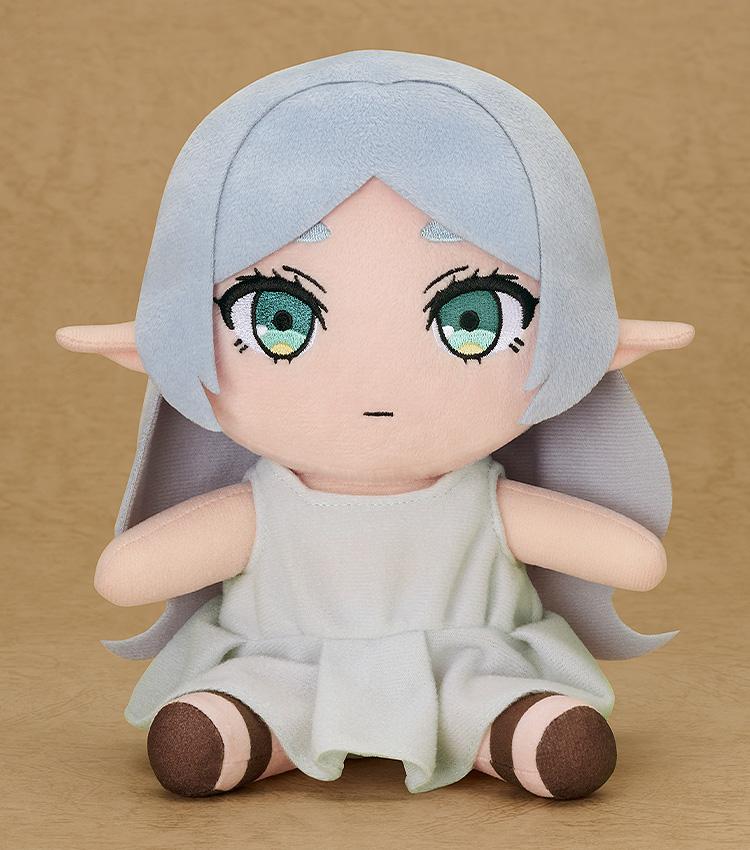 Studio shot of the 6.7-inch Frieren Apprentice Era plush sitting against a neutral tan background, showing embroidered green eyes and soft polyester texture.
