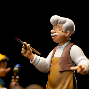 A close-up shot of the Geppetto figure from the Iron Studios Pinocchio statue, showing the hand-painted detail on his face and clothing as he holds a paintbrush.