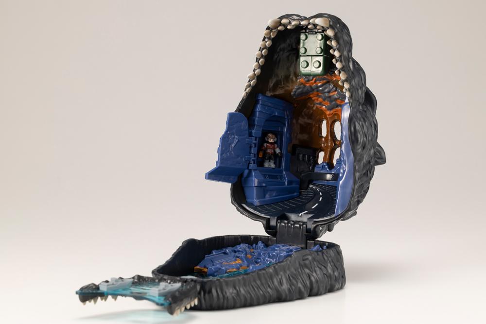 Interior of opened Godzilla pocket playset showing hinged building door and hidden pilot figure.