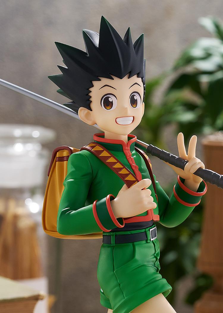 Medium close-up portrait of the cheerful Gon Freecss figure under warm ambient lighting against an antique library diorama background.