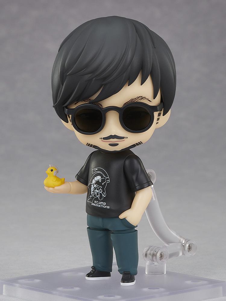 Hideo Kojima Nendoroid figure equipped with dark round sunglasses holding the yellow Ludens Duck accessory in palm.