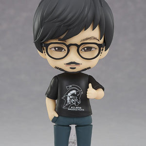 Good Smile Company Hideo Kojima Nendoroid figure wearing black Kojima Productions t-shirt and glasses in a thumbs-up pose on display stand.
