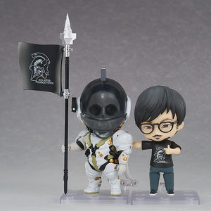 Hideo Kojima Nendoroid figure posed alongside Kojima Productions mascot Nendoroid Ludens holding a company logo spear flag.