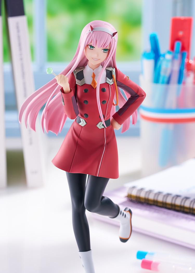 Close-up lifestyle promotional photo focusing on Zero Two's upper body, uniform detailing, and smiling expression on a desk setup.