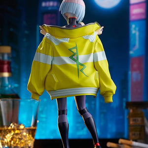 Rear view of the Lucy figure, showcasing the back of her oversized yellow jacket with the green symbol, set against a dark city skyline.