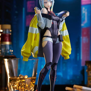 An angled frontal shot of the Lucy figure in the Night City diorama, highlighting the contrast of her dark suit against the bright moon.