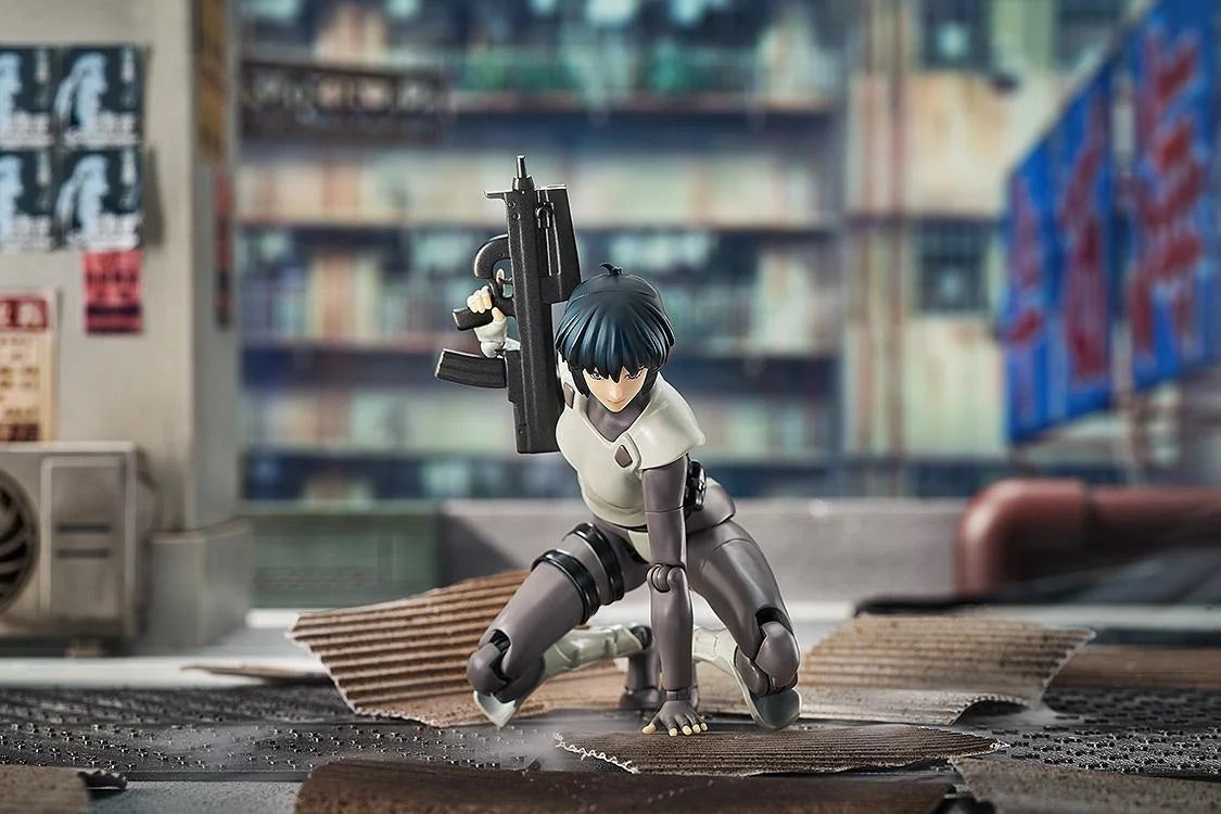 Motoko Kusanagi figure crouching on the ground in an action scene, aiming her submachine gun in an urban environment.