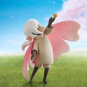 The Child of the Light figure posed on a grassy base, reaching up to the butterfly accessory, set against a bright blue sky and pink blossoms.