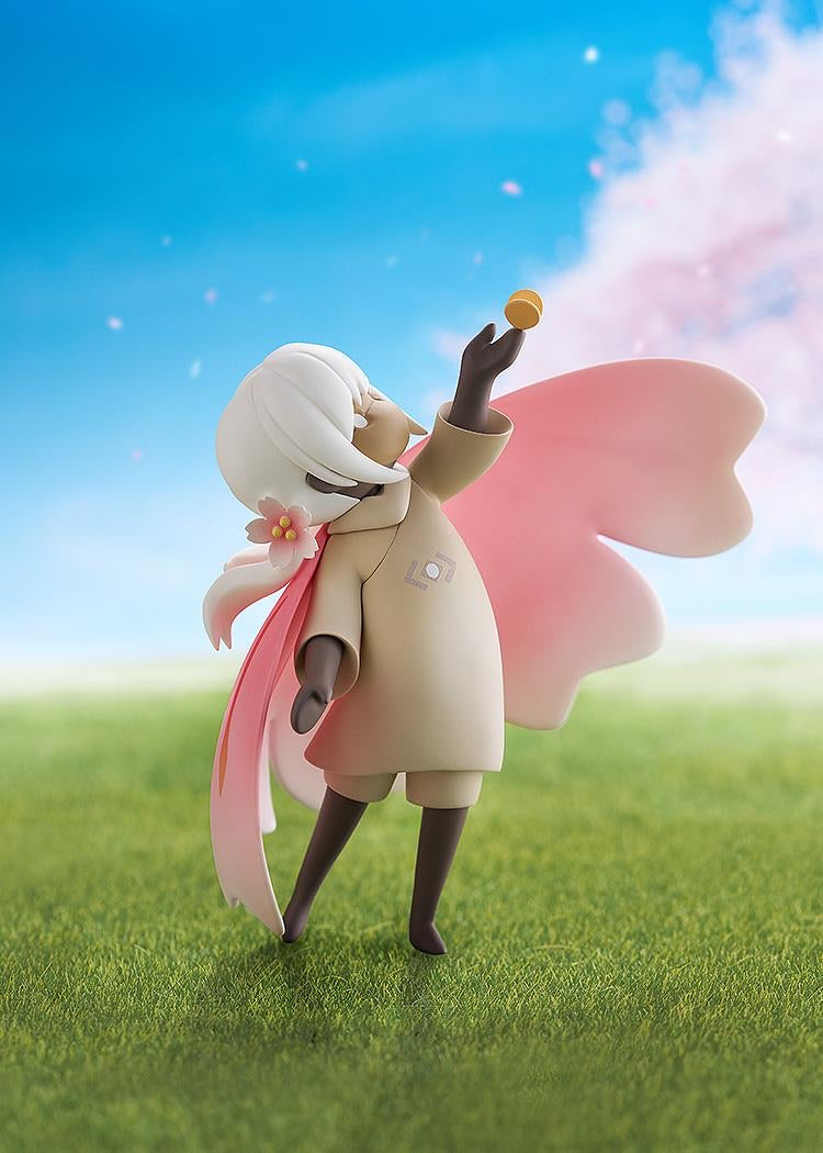 The Child of the Light figure posed on a grassy base, reaching up to the butterfly accessory, set against a bright blue sky and pink blossoms.