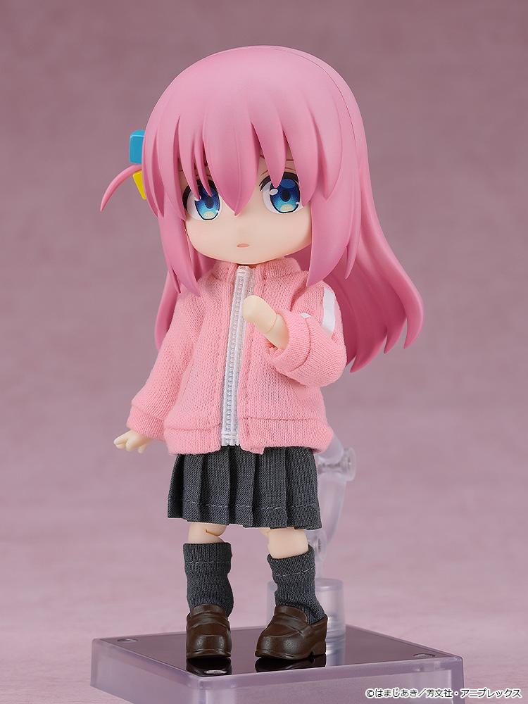 Full body front view of the highly articulated Hitori Gotoh Nendoroid Doll reissue figure standing on a clear plastic display base against a soft pink background.