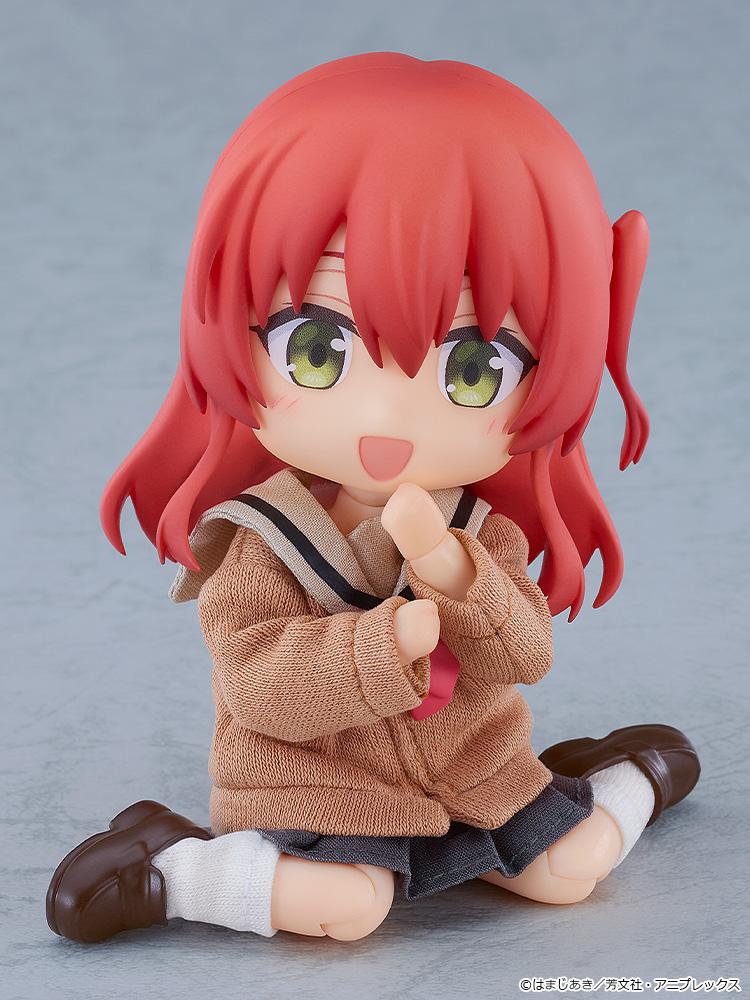Cute floor-sitting pose of the highly articulated Ikuyo Kita Nendoroid Doll figure resting with her hands near her face and a happy expression.