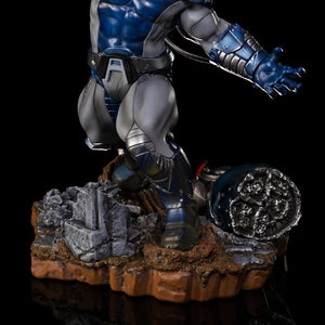 A close-up of the lower half of the Apocalypse statue, highlighting his armored legs and the rubble-strewn base with destroyed Sentinel parts.