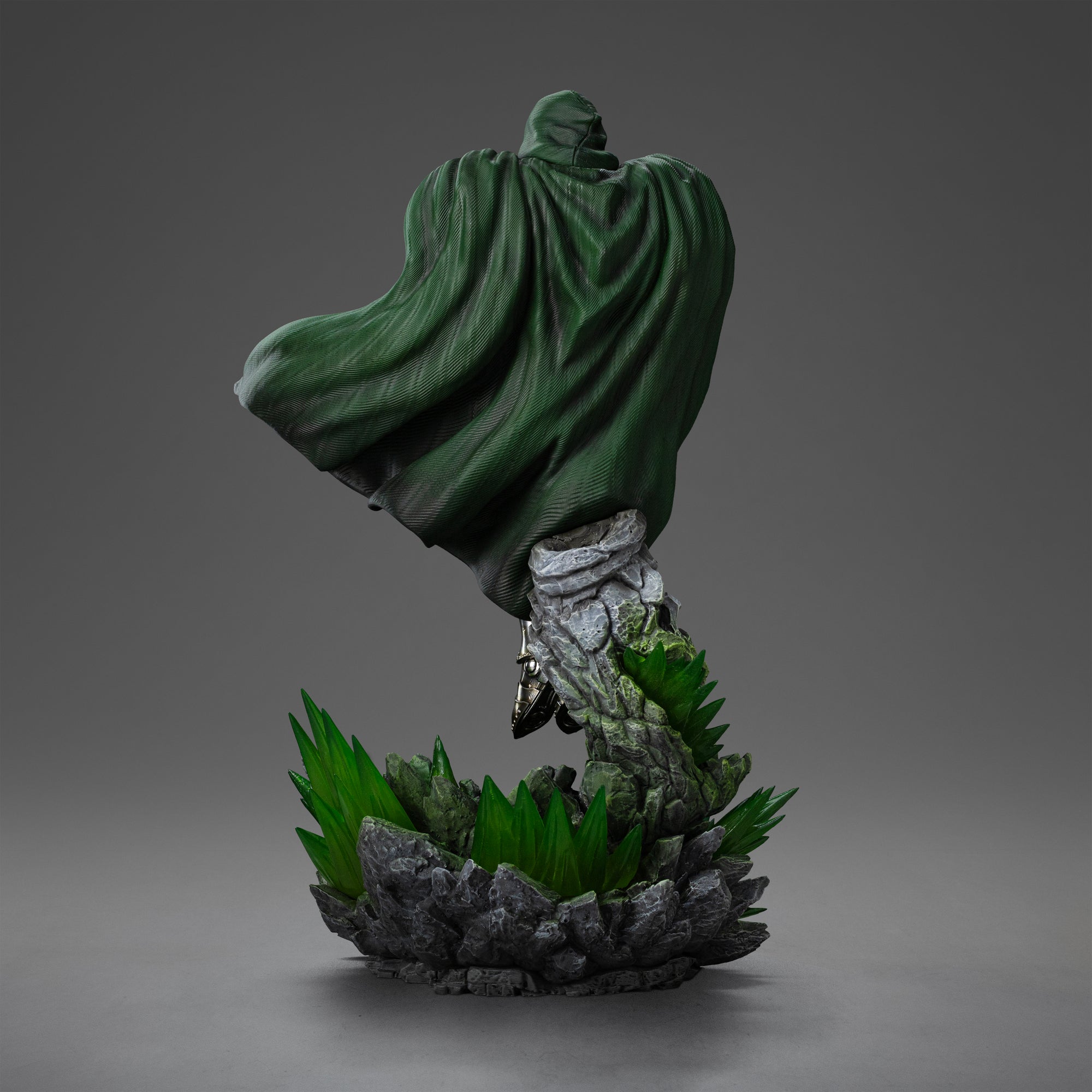 Rear view of the Doctor Doom statue, showcasing the flow and texture of his green fabric cape and the rocky base below.