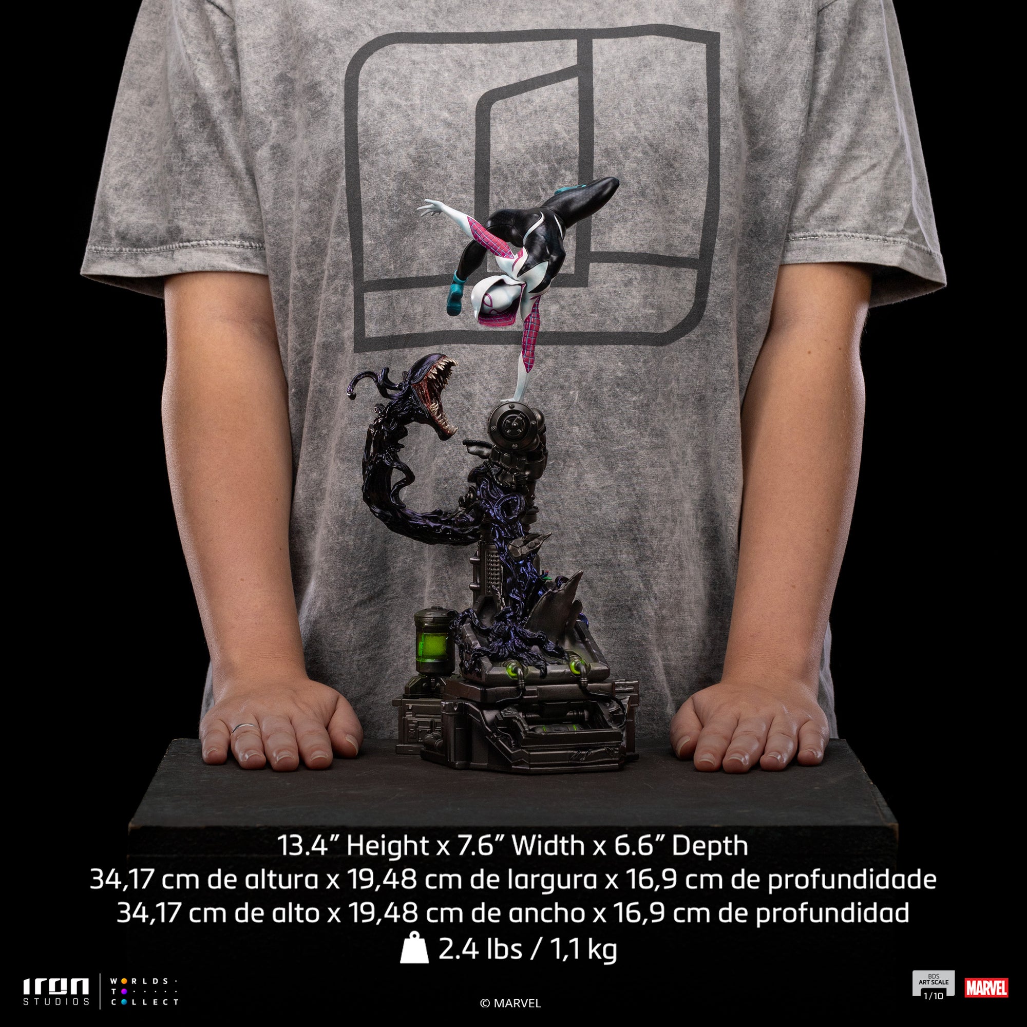 A size comparison photo of the Iron Studios Ghost-Spider 1/10 Scale Statue held by hands, with its 13.4-inch height, 7.6-inch width and 6.6" depth dimensions listed.