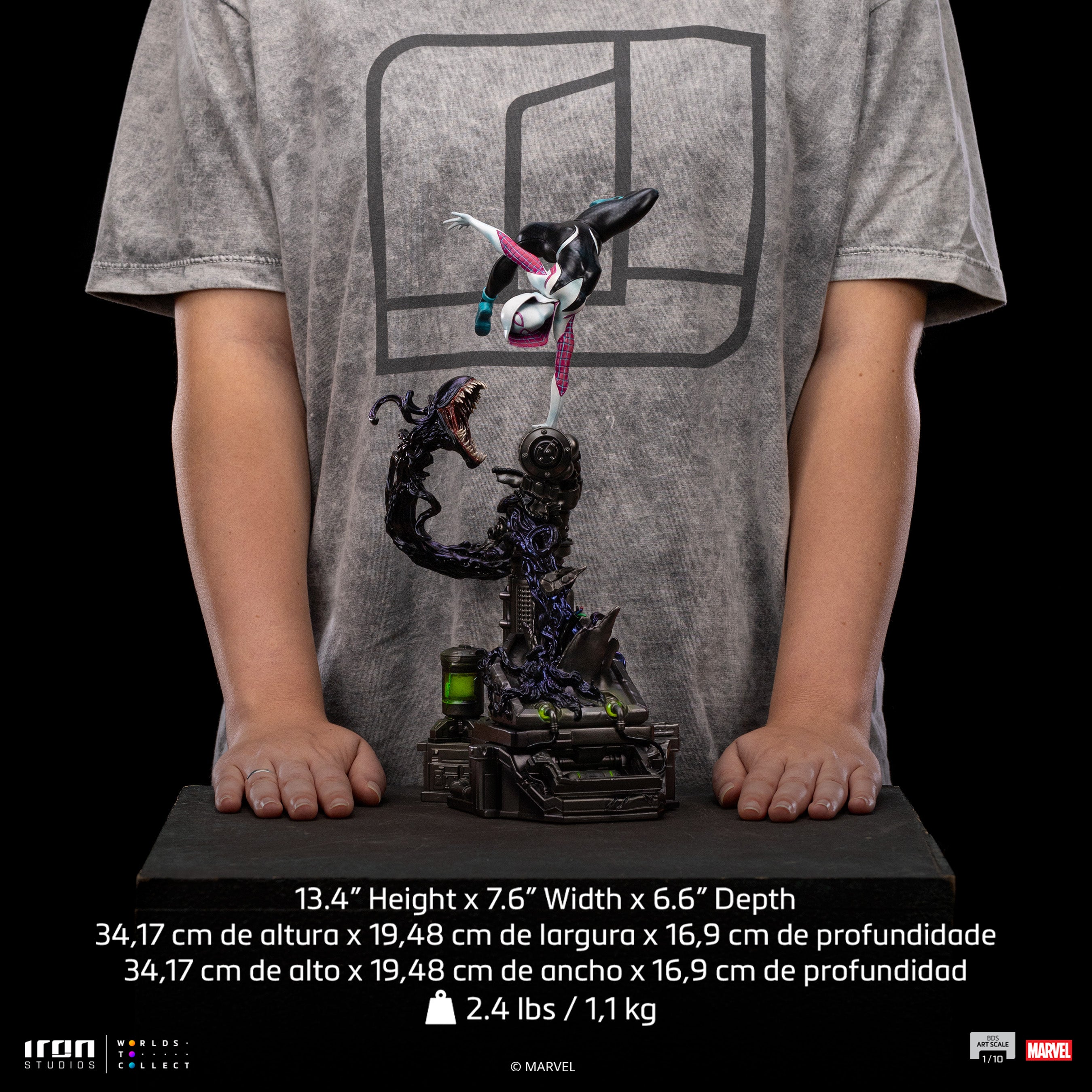 A size comparison photo of the Iron Studios Ghost-Spider 1/10 Scale Statue held by hands, with its 13.4-inch height, 7.6-inch width and 6.6" depth dimensions listed.