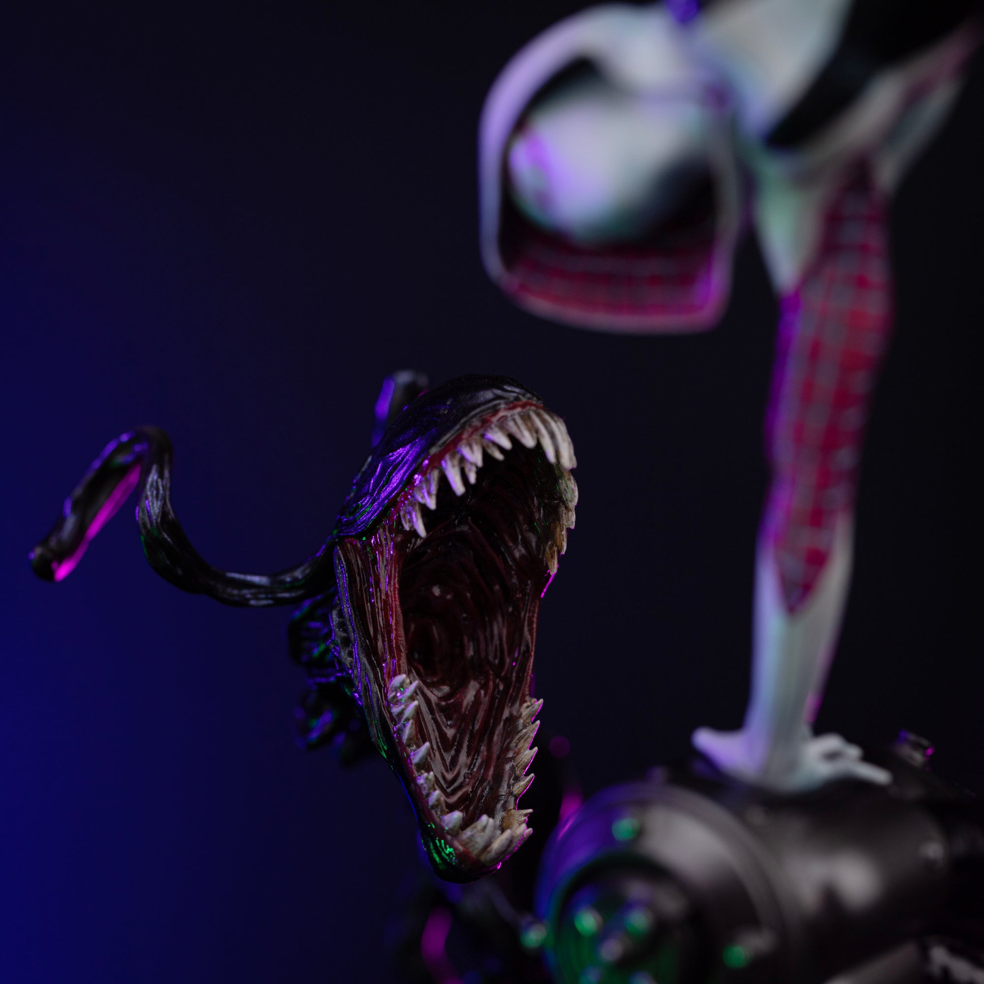 A close-up of the symbiote tendril's open, fanged mouth on the base, set against a dark background with blue and magenta lighting.