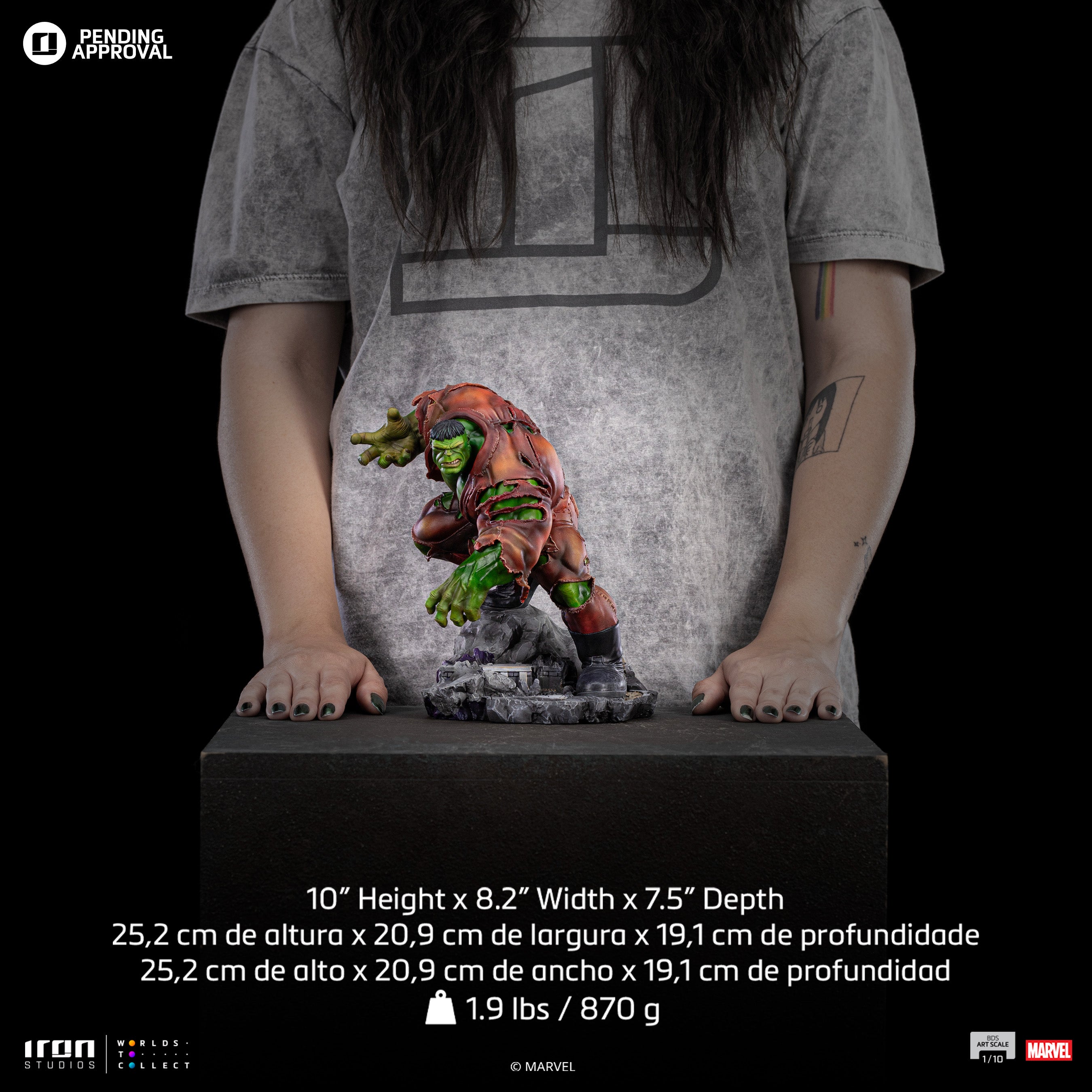 A size comparison photo of the Iron Studios Hulk 1/10 Scale Statue in front of a person, their hands by its side, with its 10-inch height, 8.2-inches width and 7.5-inches depth.