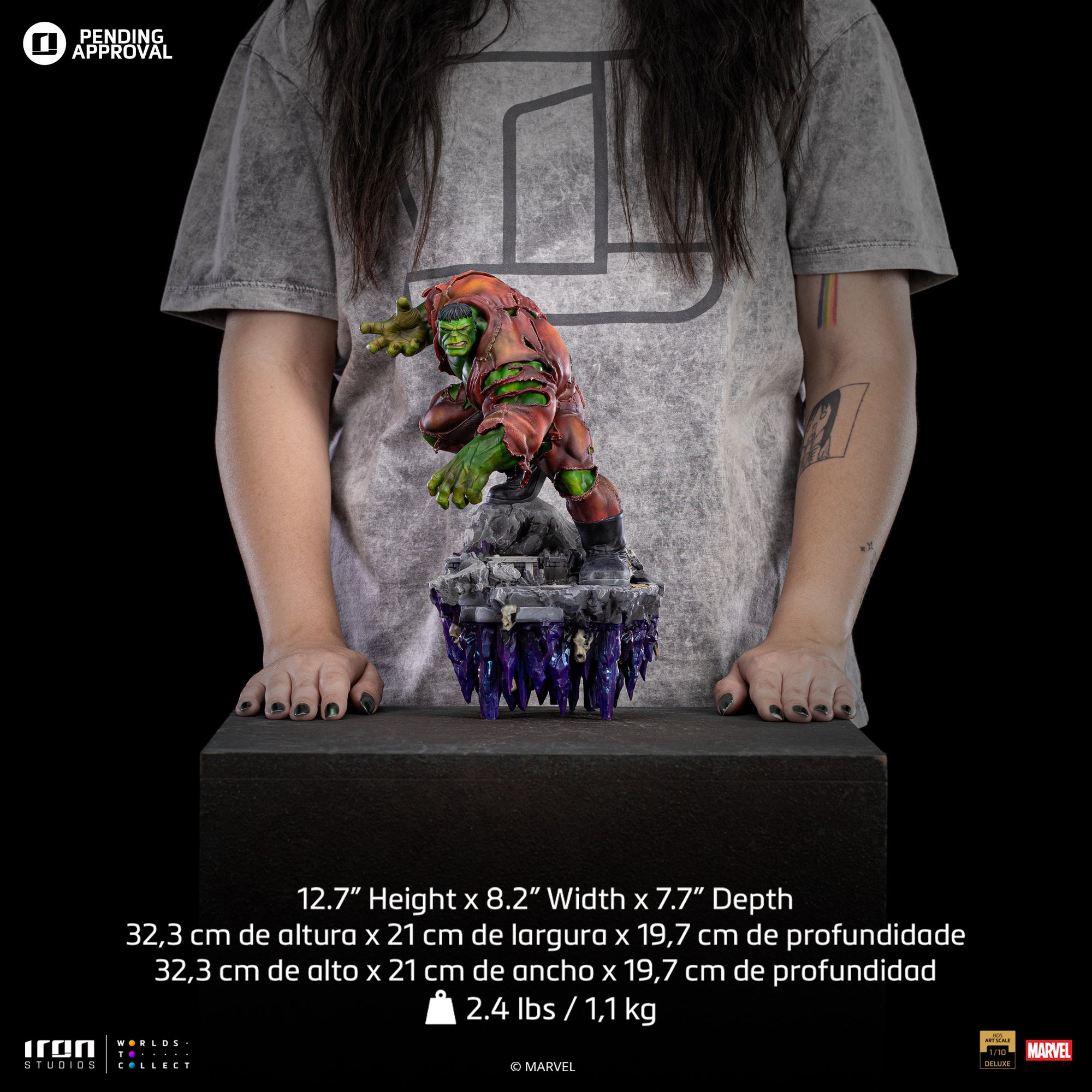A size comparison photo of the Iron Studios Hulk Deluxe 1/10 Scale Statue standing in front of a person with their hands resting by the side of the statue, with its dimensions listed as 12.7-inch height, 8.2" width, and 7.7" depth.