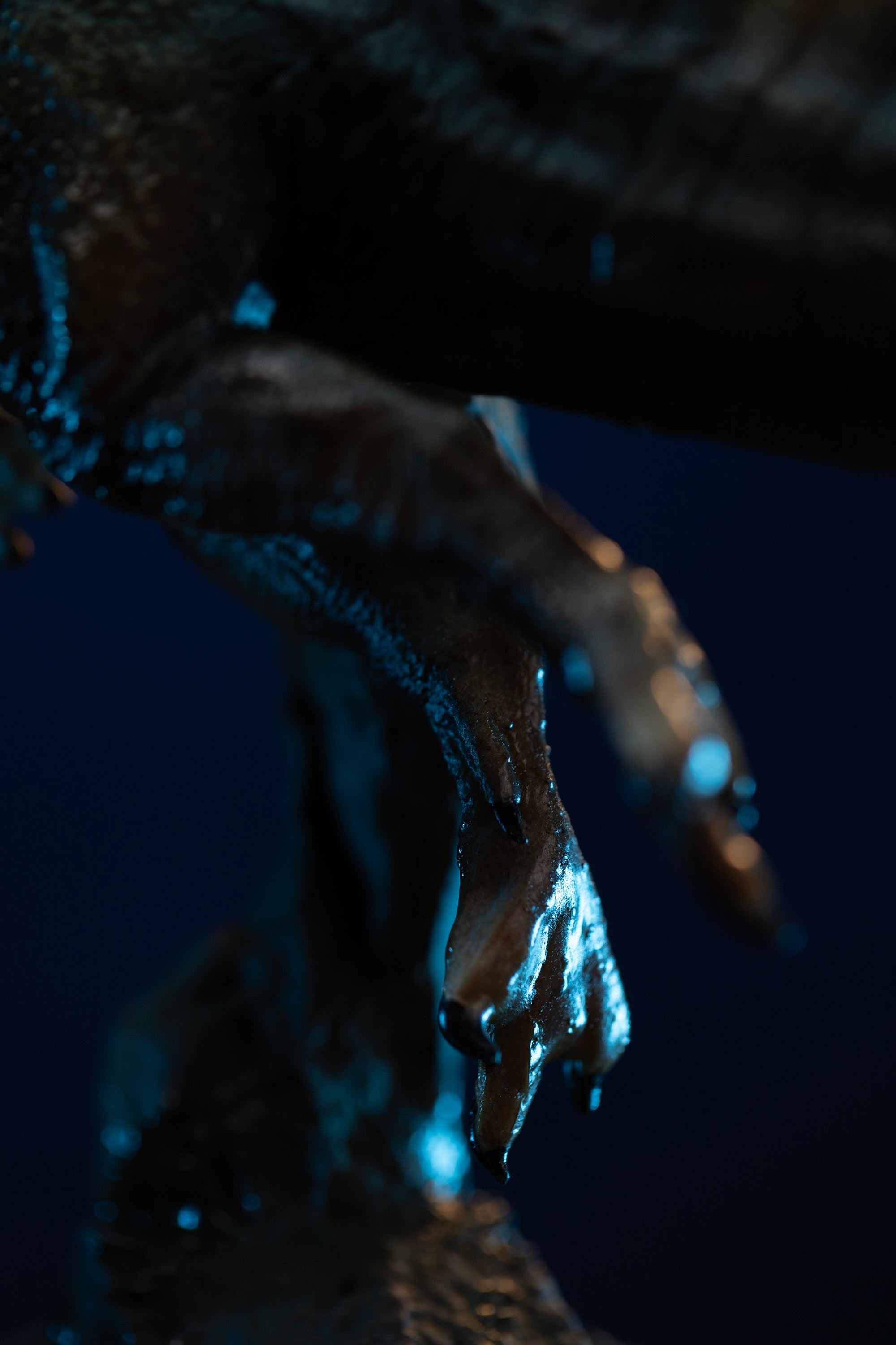 Macro detail of Iron Studios Spinosaurus statue webbed clawed feet and skin texture under blue light