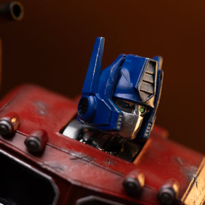Extreme close-up of Optimus Prime's blue helmet crest, silver faceplate, and green optic eyes on the Iron Studios statue.