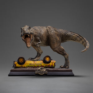 Front view of the Iron Studios Icons line T-Rex Attack polystone statue from Jurassic Park, featuring a Tyrannosaurus Rex roaring with an open mouth while stepping on an overturned yellow tour vehicle on a black base.