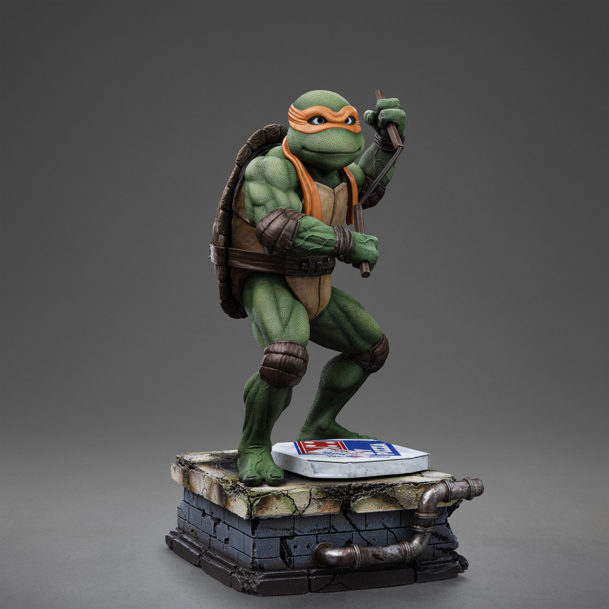 Right three-quarter studio view of the Iron Studios TMNT 1990 Michelangelo 1/10 scale statue holding nunchaku on a sewer base.