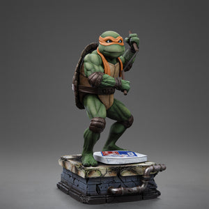 Right three-quarter studio view of the Iron Studios TMNT 1990 Michelangelo 1/10 scale statue holding nunchaku on a sewer base.