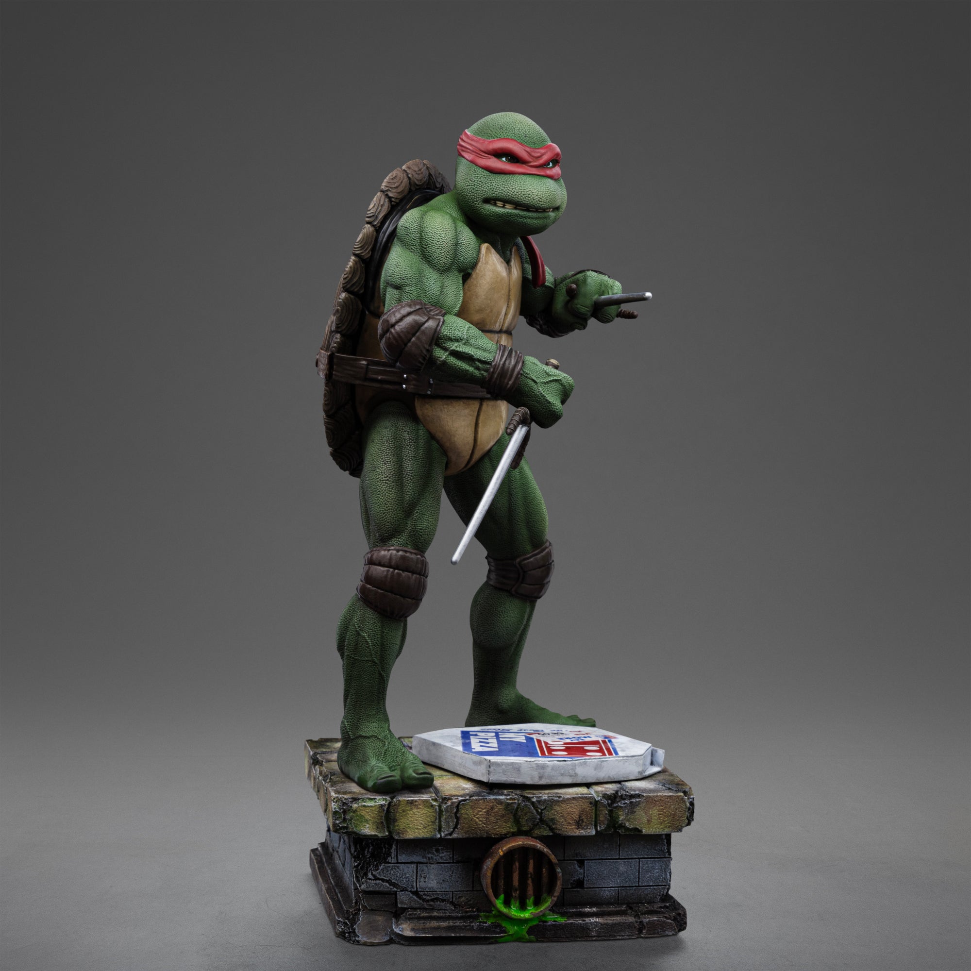 Right three-quarter studio view of the Iron Studios TMNT 1990 Raphael 1/10 statue wielding sai daggers on a sewer brick base.