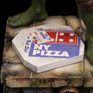 Close-up of the vintage NY Pizza box accessory resting on the weathered stone sewer base of the Iron Studios Raphael statue.